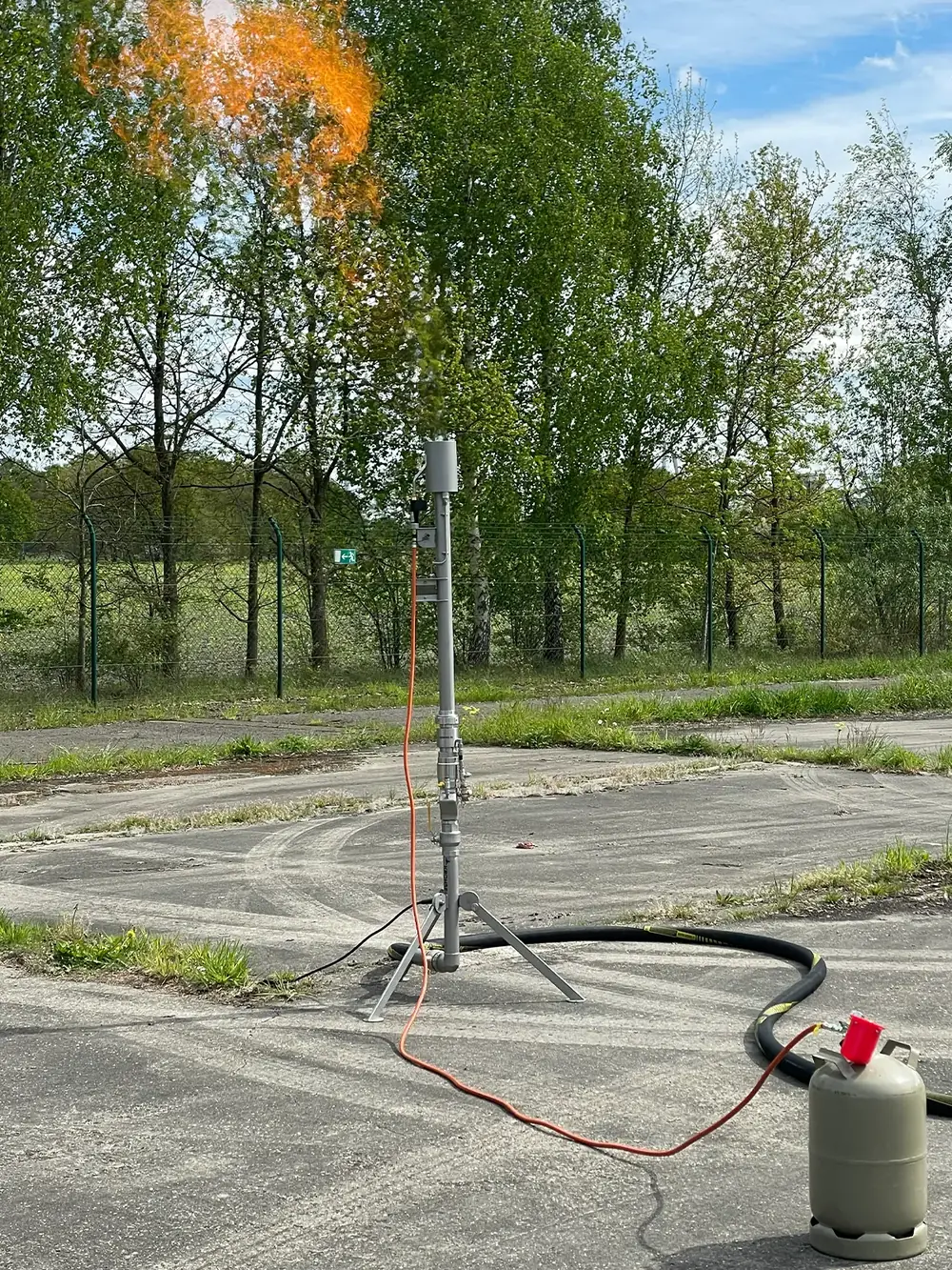Gasfackel auf einer Betonfläche, daneben die Propanflasche für die Zündflamme.