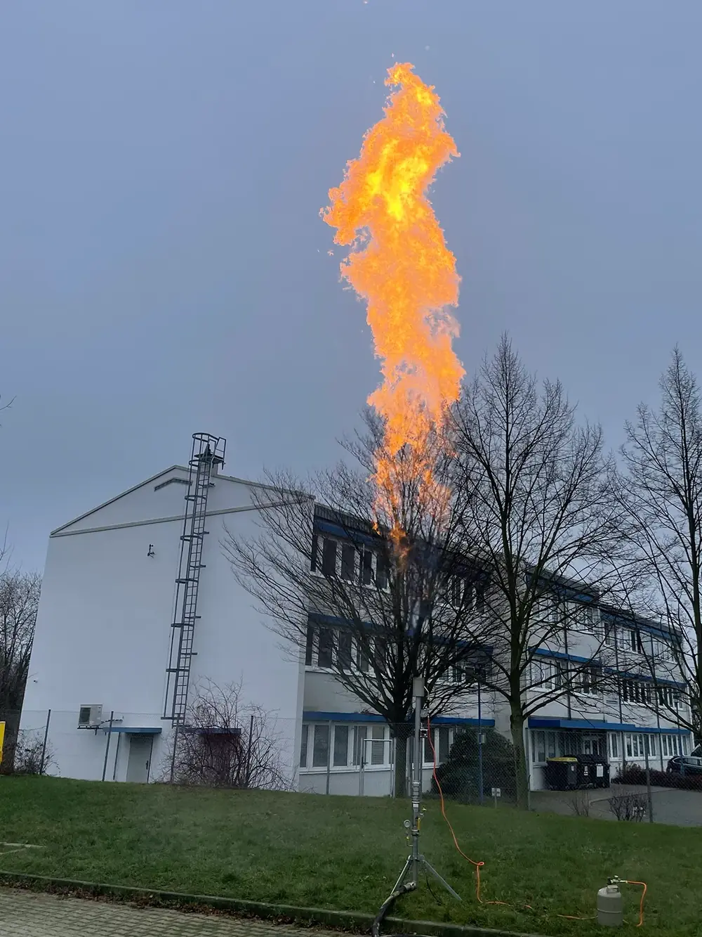 Gasfackel vor einem Betriebsgebäude, die Flamme reicht über das Dach.