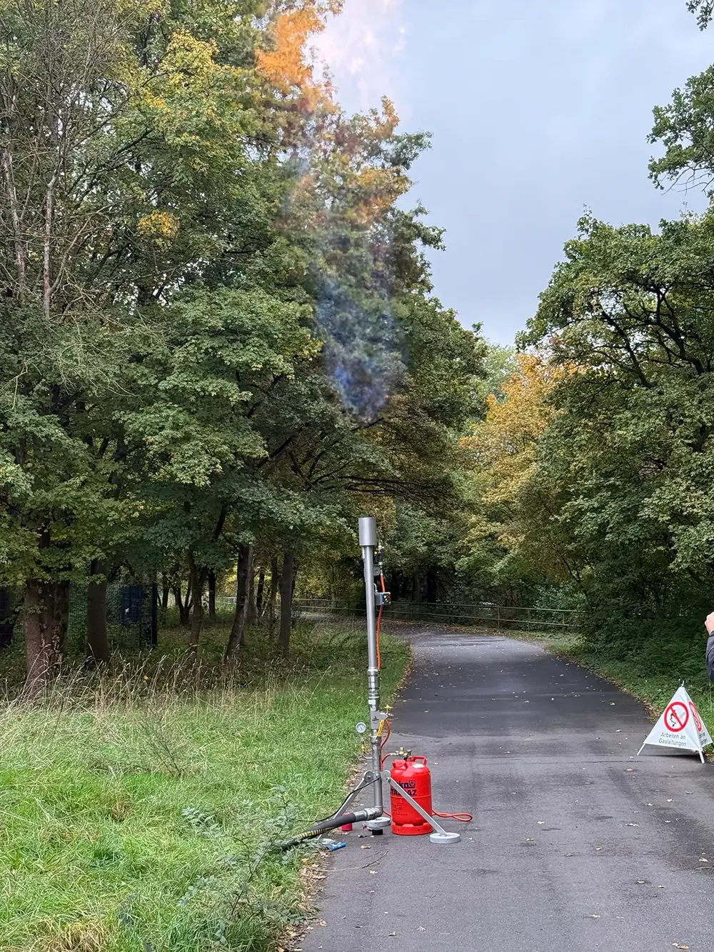 Gasfackel am Rand eines Waldwegs, mit Feuerlöscher und Warnschild abgesichert.
